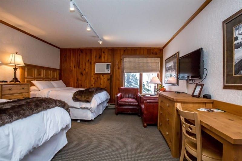 Hotel room with two beds, wooden paneling, and a desk. Includes a window and a red armchair.