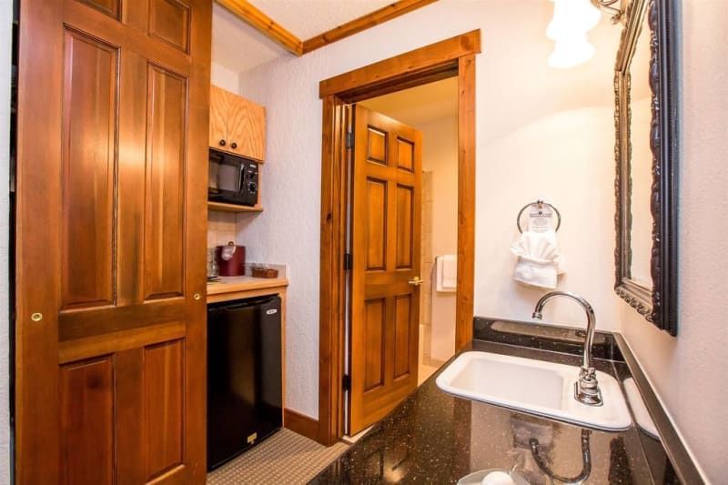 Small kitchenette with a sink, mini-fridge, microwave, and an open doorway to a bathroom. Wooden cabinets and trim.