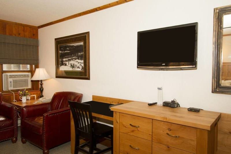 A hotel room featuring a leather chair, dresser with TV, artwork, and window with an AC unit.