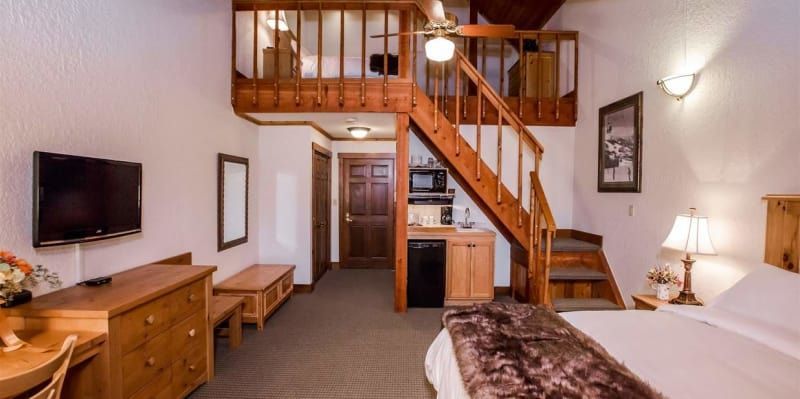A hotel room with a loft area, featuring a wooden staircase, furnishings, and a kitchenette.
