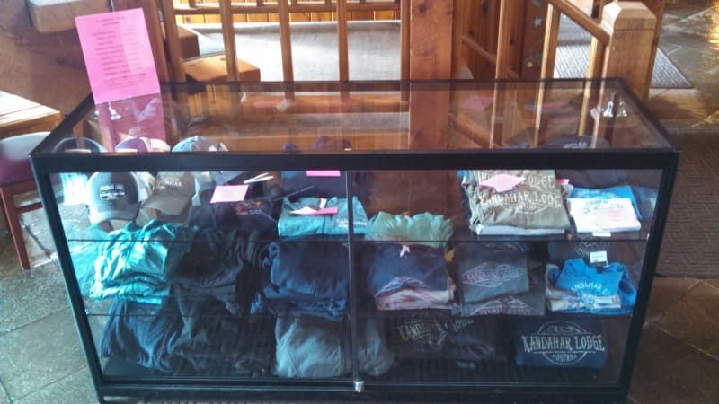 A glass display case filled with folded t-shirts and hats, likely for sale, inside a wooden building.