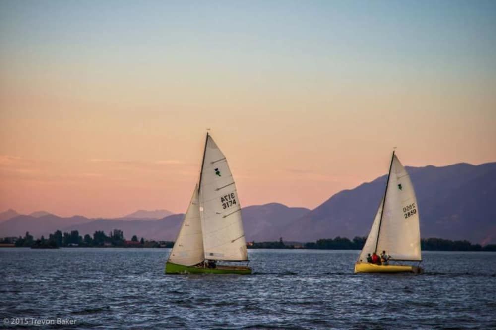 Two sailboats on a lake with a mountain range in the background at sunset.