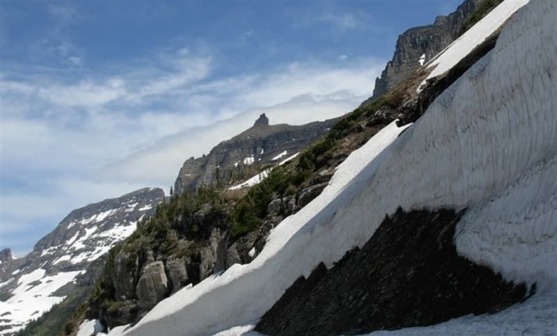 Snowy mountain slope with rocky peaks under a partly cloudy sky.