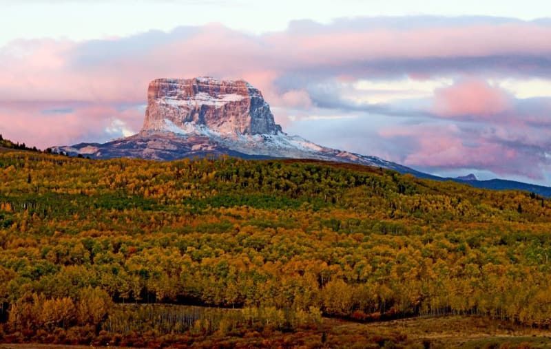 Autumn forest and mountain peak at sunset with pink and purple sky.