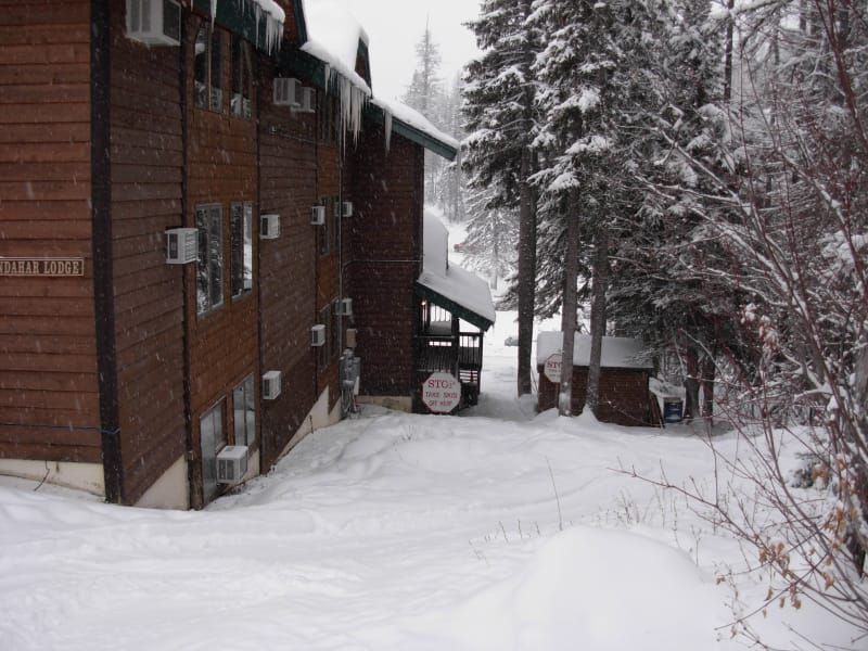 Snow-covered wooden lodge in a forest. Snow blankets the ground and clings to evergreen trees.