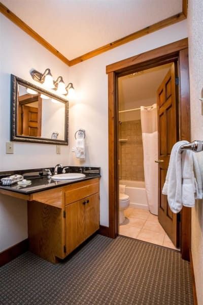 Bathroom with dark countertop, wood cabinets, and a partially open door to a shower/tub. White walls, wood trim, and a dark patterned floor.