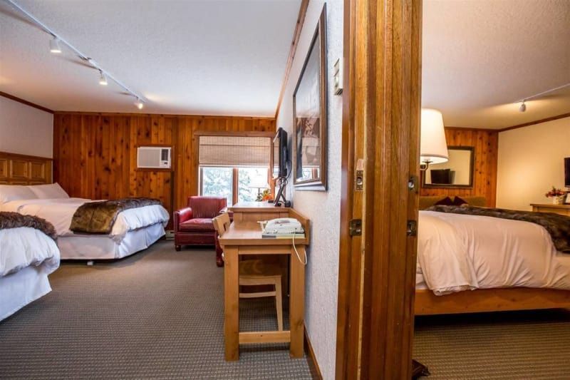 Hotel room with two beds visible, along with a small desk, chair, and window. The walls are wooden.