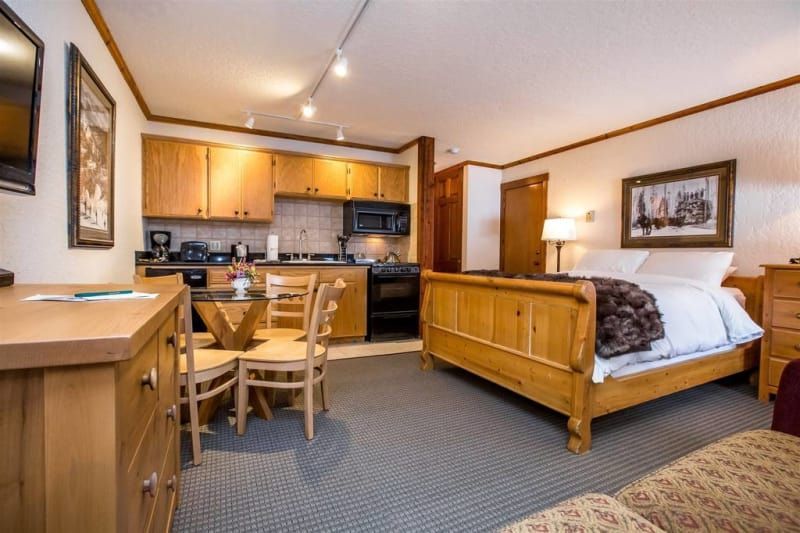 Small studio apartment with a kitchen, dining table, bed, and seating area; wood furniture and trim.