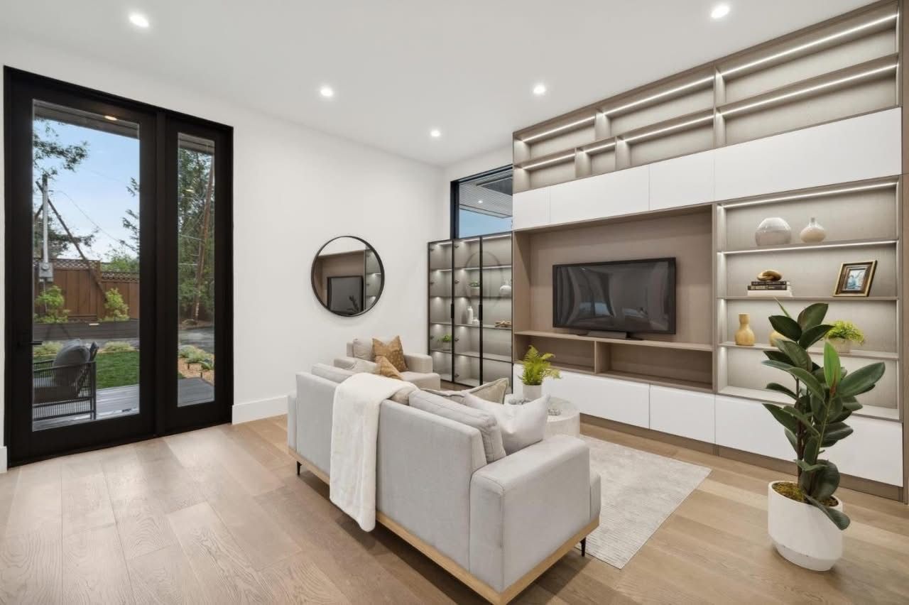 Modern bright living room with white sofa, wood floors, TV wall, and large glass doors