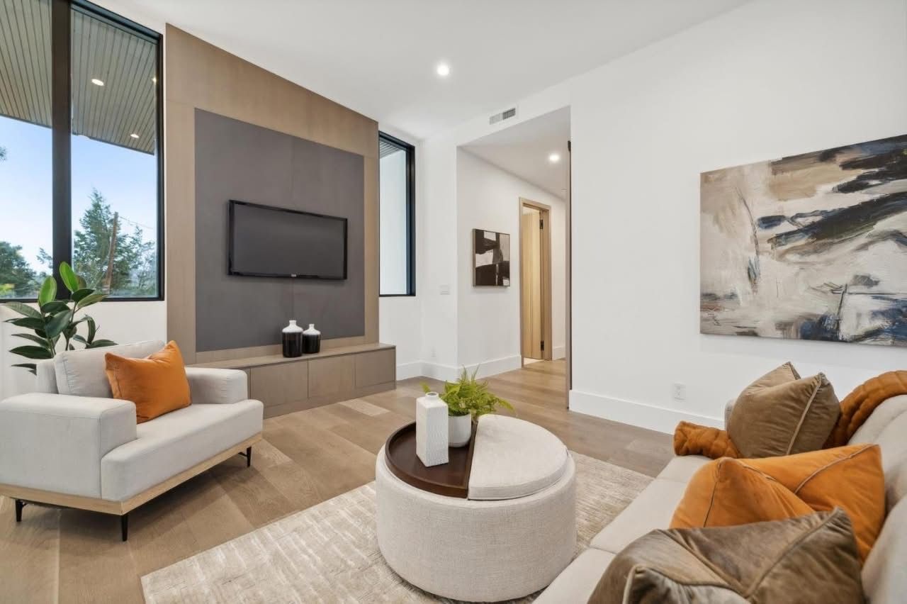 Modern living room with white sofas, orange accents, wall-mounted TV, and large windows