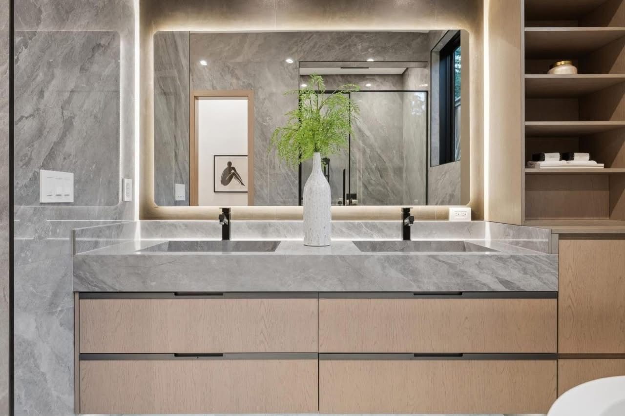 Modern marble bathroom vanity with double sinks, backlit mirror, and a vase of greenery