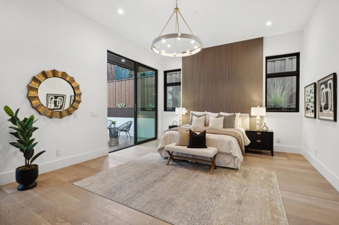 Bright modern bedroom with a large bed, beige rug, pendant light, and sliding glass doors to a patio.