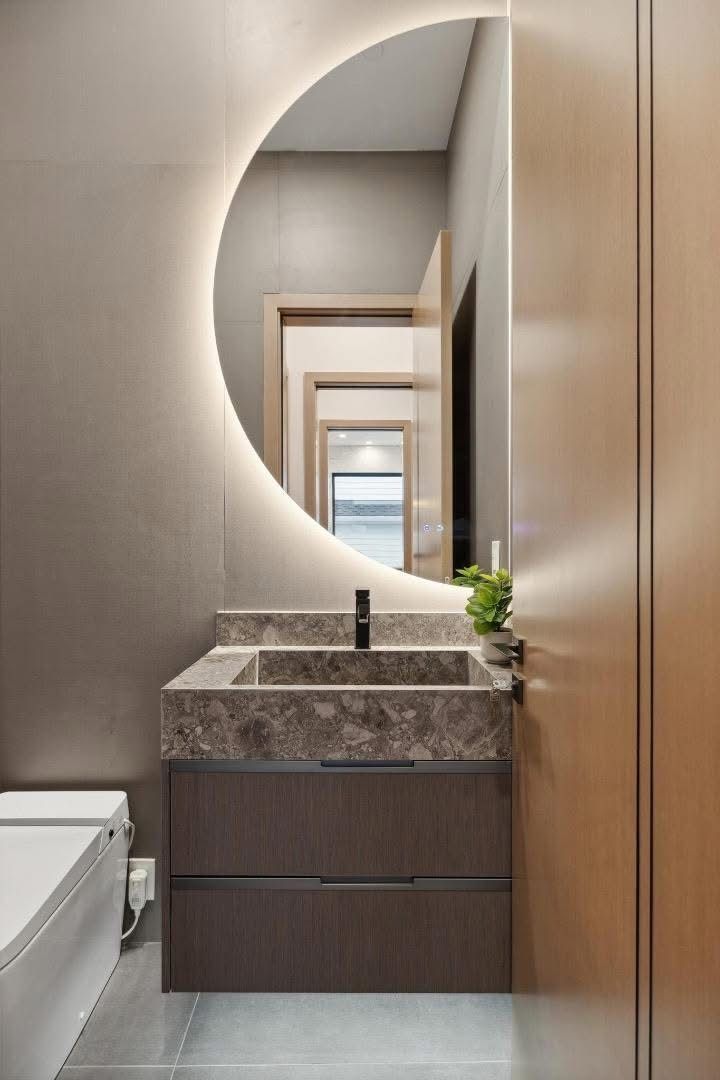 Narrow modern bathroom with floating vanity, marble sink, and backlit round mirror