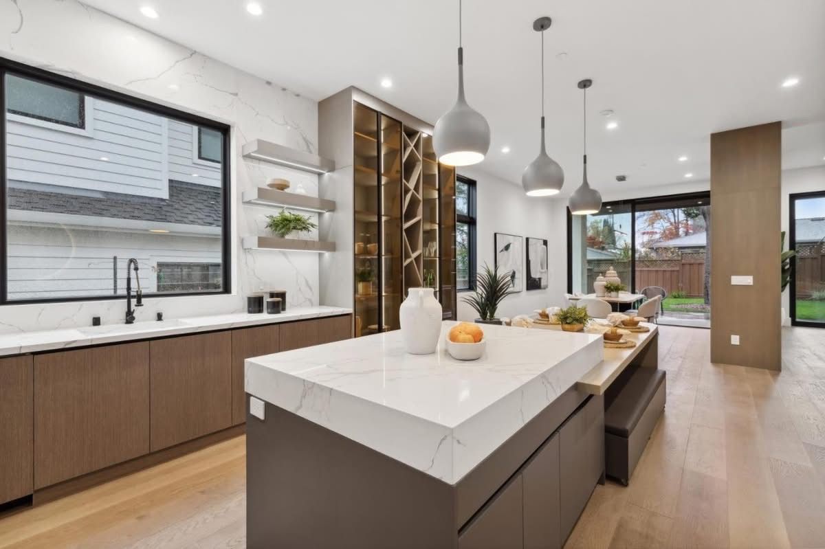 Modern open-plan kitchen with white island, pendant lights, wood cabinetry, and large window