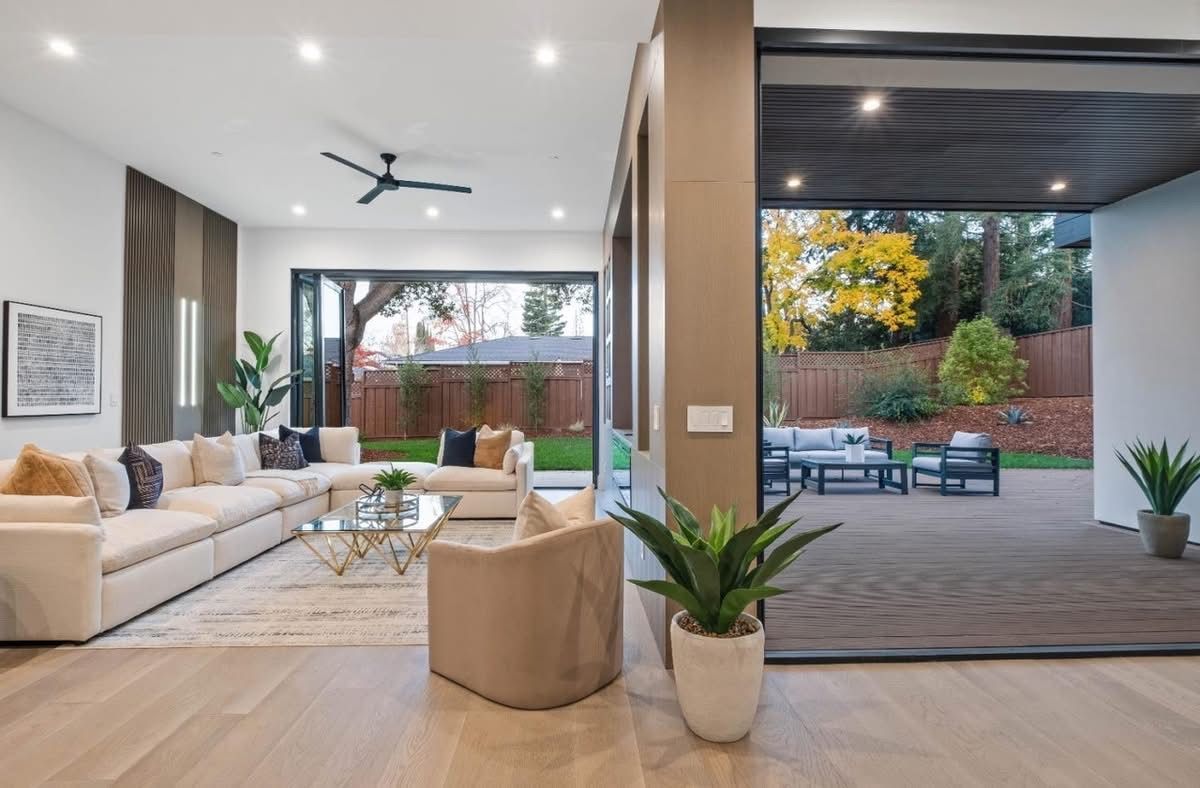 Modern living room opening to a covered patio with outdoor seating and garden views