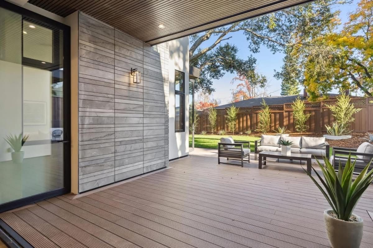 Modern patio with wood decking, lounge chairs, potted plant, and a sliding glass door under a covered overhang