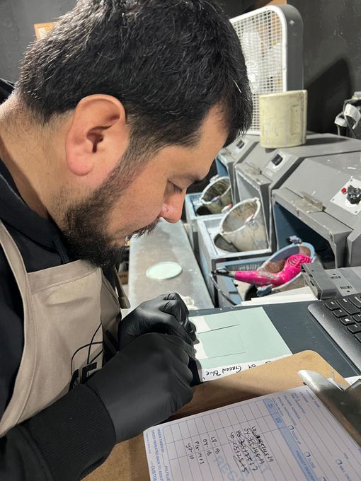 Man in gloves carefully working at a desk with tools and papers in a workshop-like setting