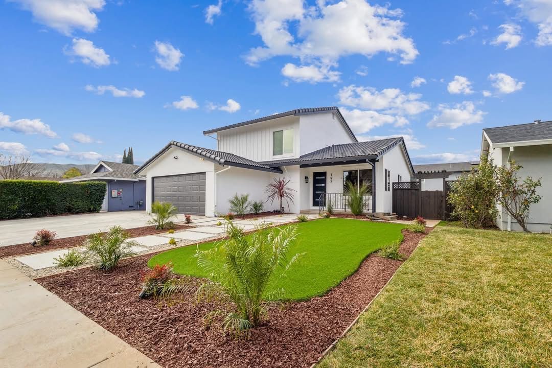 Modern suburban house with a two-car garage, landscaped front yard, and blue sky with clouds