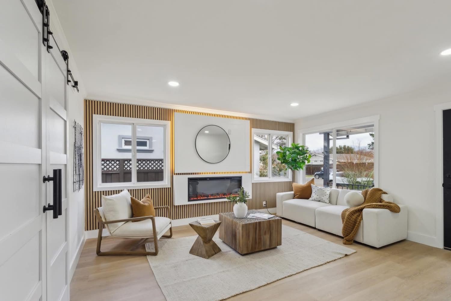 Modern bright living room with white sofa, fireplace, large mirror, and wood accents