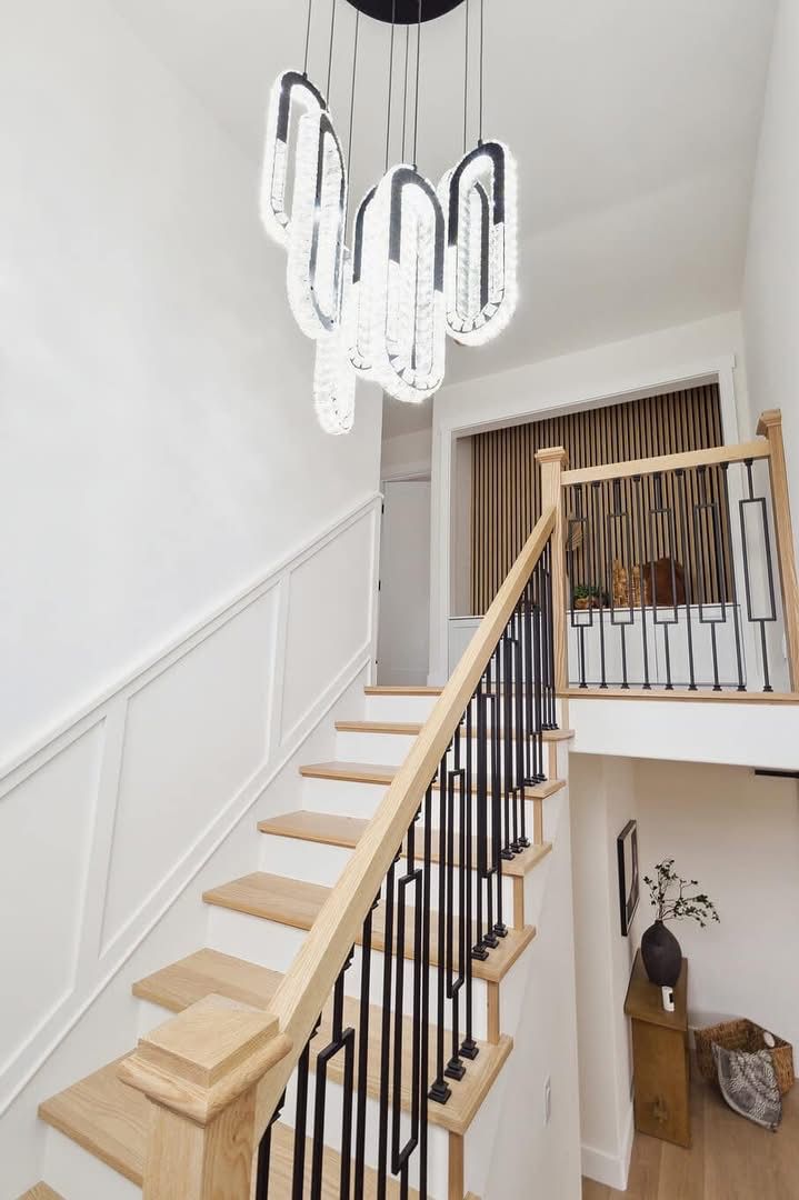 Modern staircase with light wood steps, black railings, and a white sculptural chandelier in a bright entryway