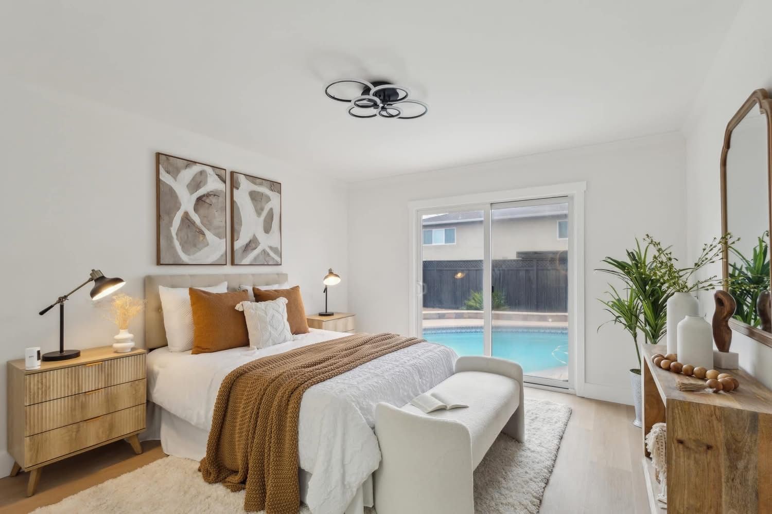 Bright bedroom with a bed, woven bench, wood accents, and sliding doors to a pool outside
