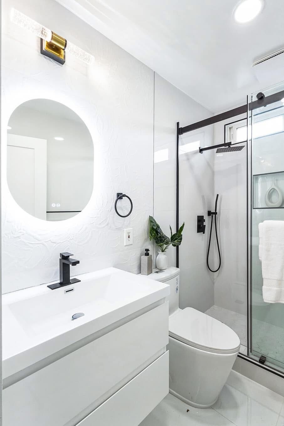 Modern white bathroom with sink, round mirror, toilet, and glass shower stall