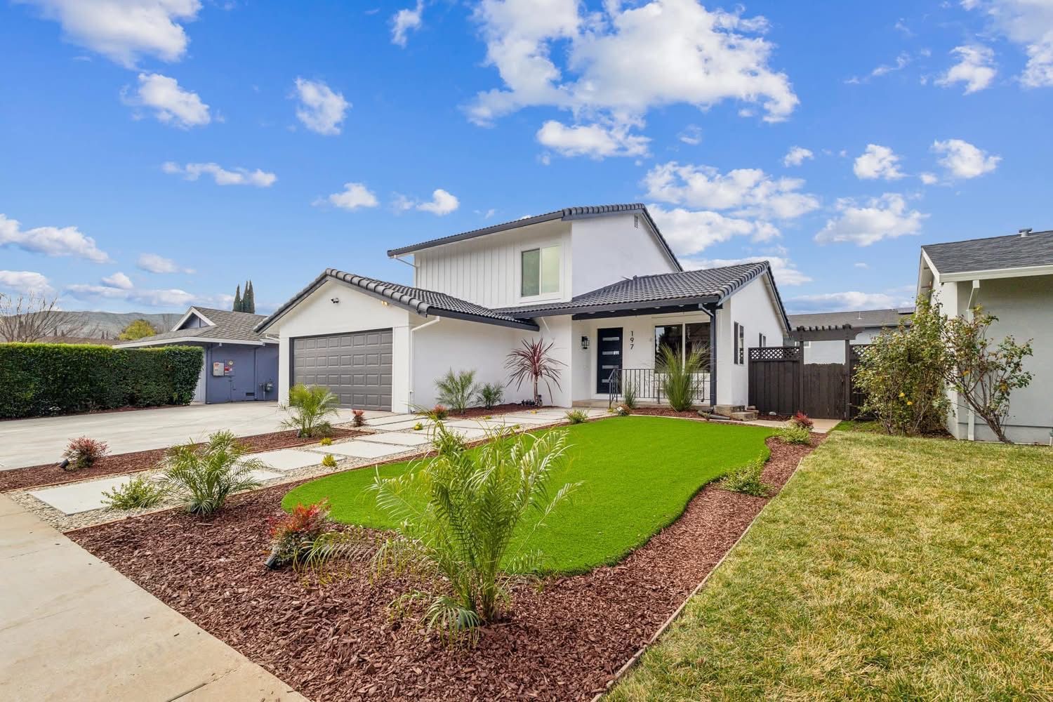 Modern suburban house with a manicured front yard, driveway, and blue sky with clouds