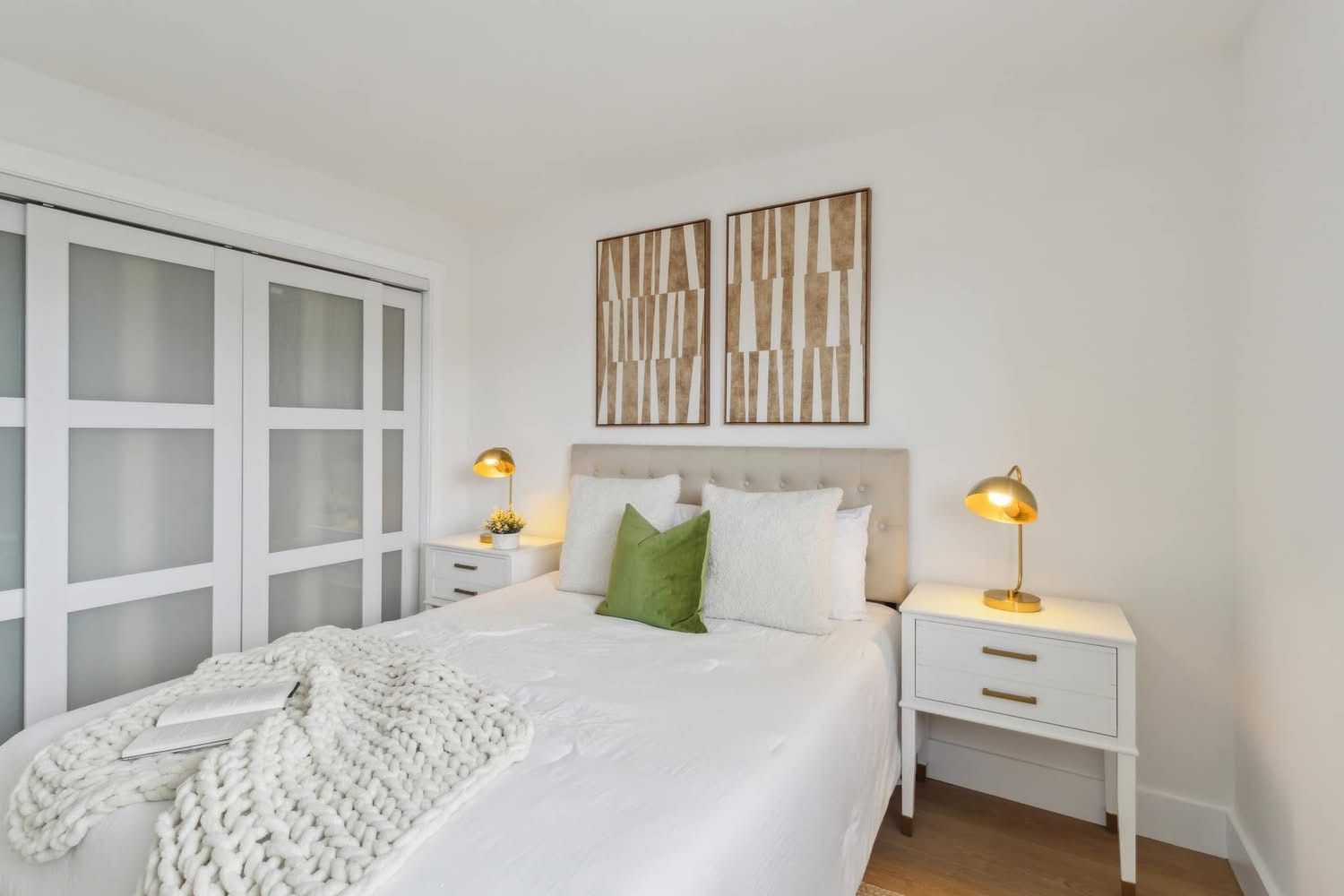 Bright white bedroom with a neatly made bed, bedside lamps, and minimalist wall art