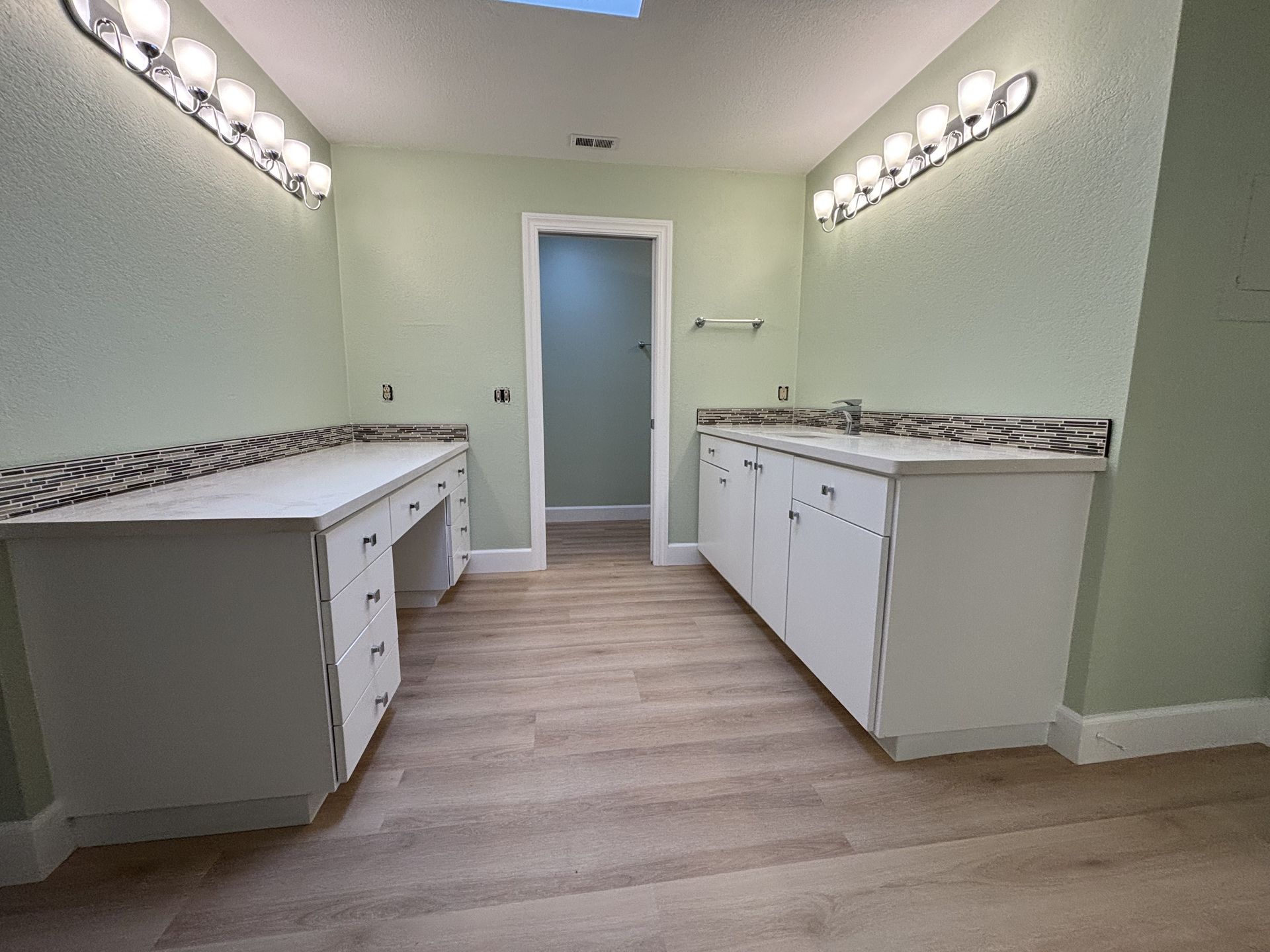 Empty double vanity bathroom with green walls, white cabinets, and mirrors above both sinks.