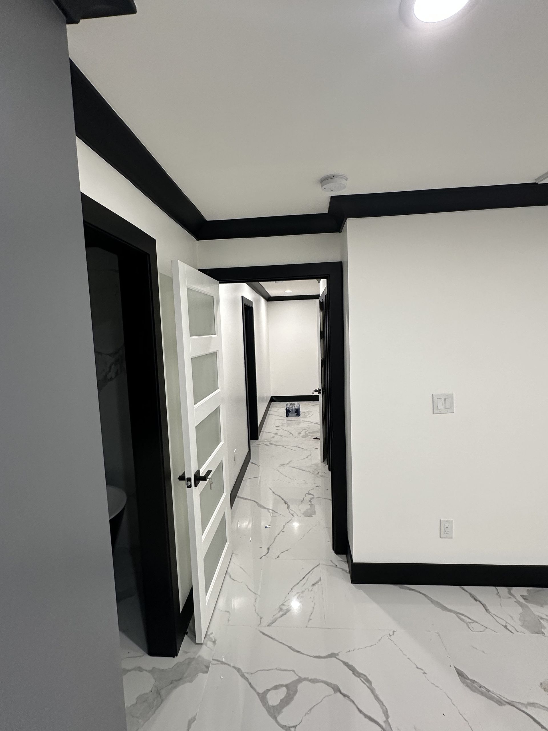 Bright hallway with white marble floor, black trim, and glass-paneled doors.