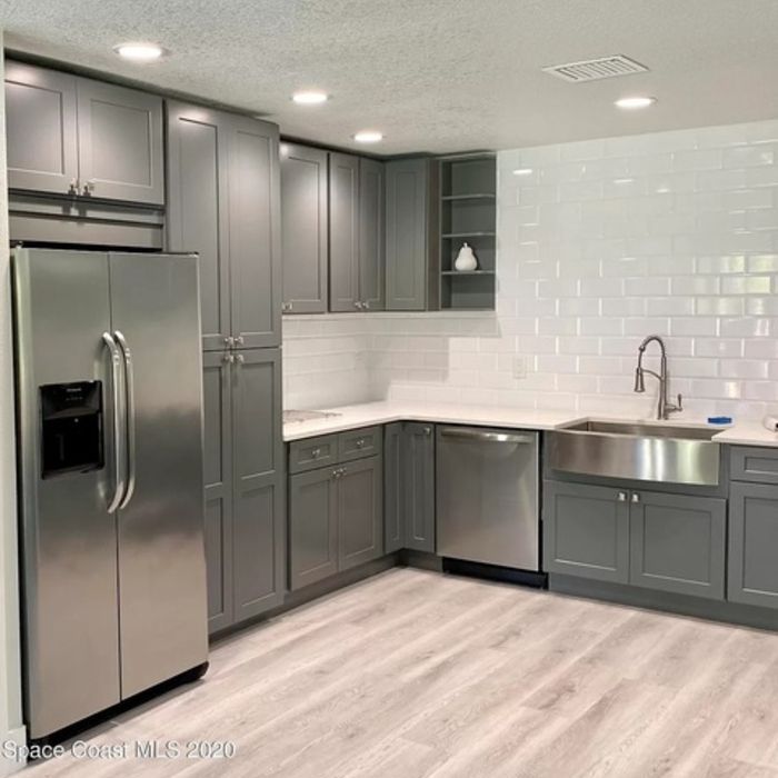 Gray kitchen with stainless steel appliances, white subway tile backsplash, and light wood-look flooring.