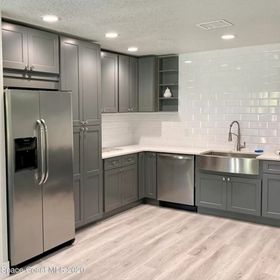 Gray kitchen with stainless steel appliances, white tile backsplash, and light wood-look flooring.