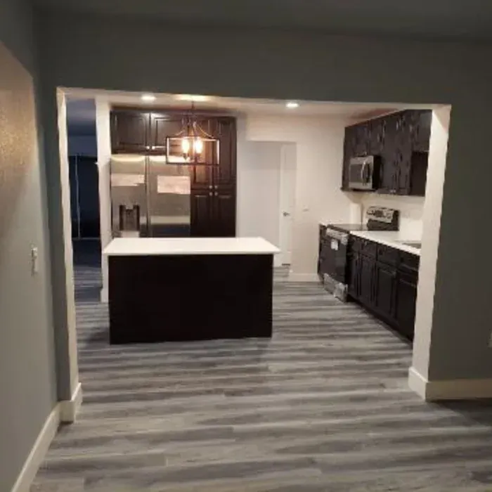 Kitchen with dark cabinets, white countertop island, and wood-look flooring.
