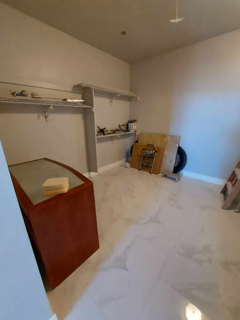Empty, light-colored room with white tiled floor, shelving, and a red cabinet, possibly a closet or storage space.
