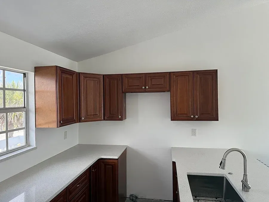 Kitchen with dark wood cabinets, white countertops, and a stainless steel sink.