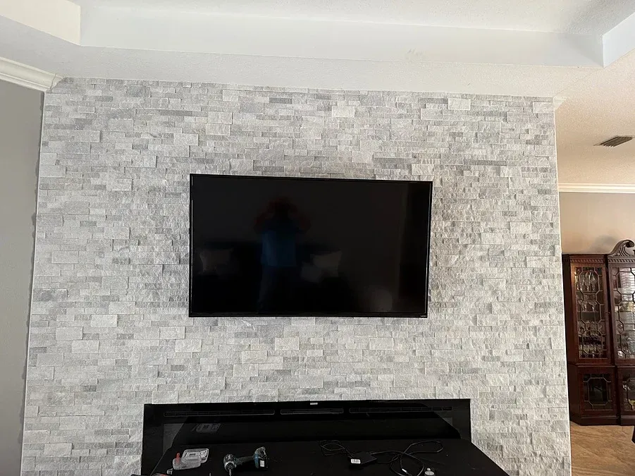 TV mounted on a gray stacked stone wall above a black fireplace.