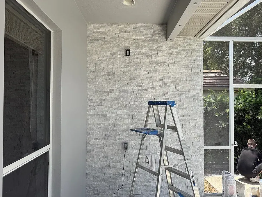 Gray stone wall with a ladder and a person working next to a screened enclosure.