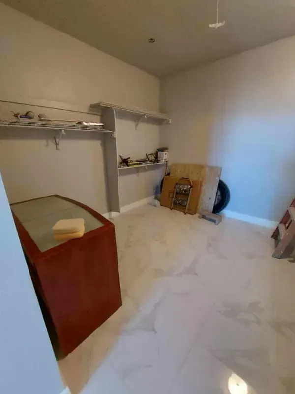 A small room with white tiled floor, shelving, and red cabinet. Construction materials are also present.