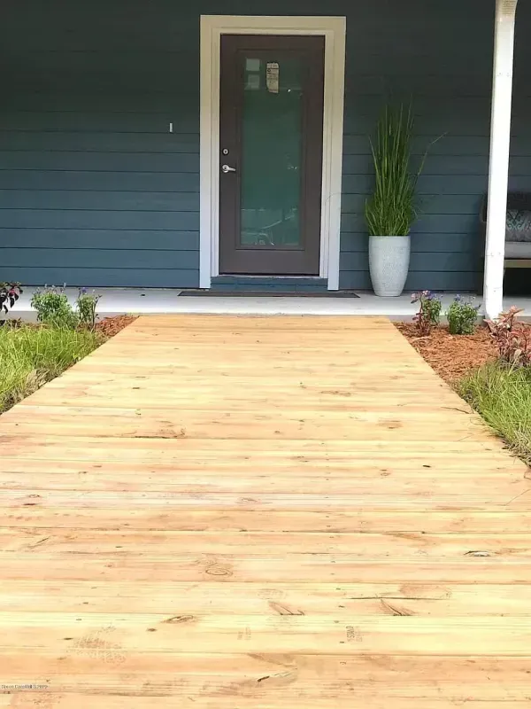 Wooden walkway leading to a house with a blue exterior and brown door.