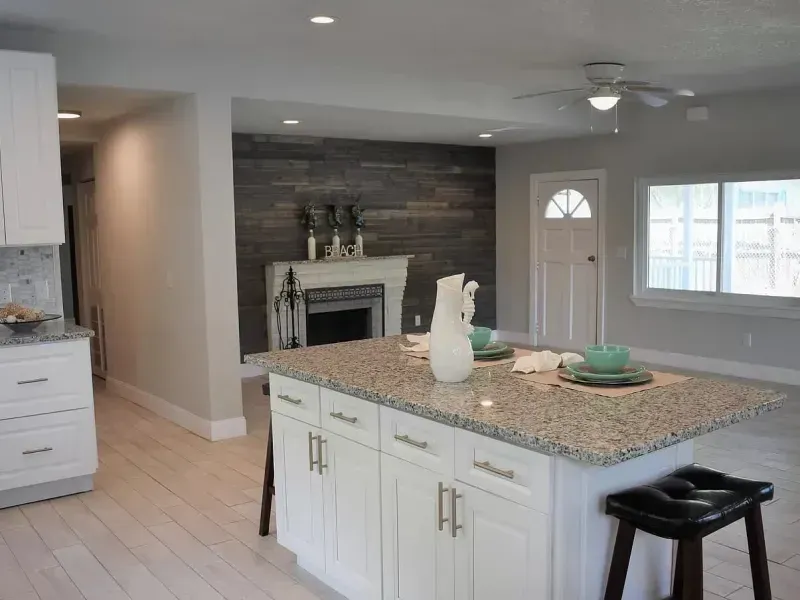 Modern open-plan kitchen with a stone island and fireplace in the living area. Light wood flooring, white cabinets.