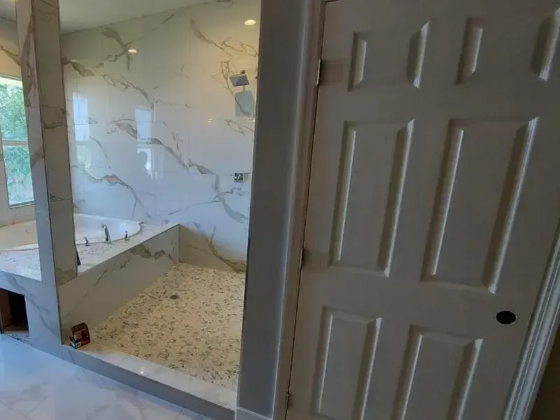 Modern bathroom with a tiled shower, white door, and marble-like walls.