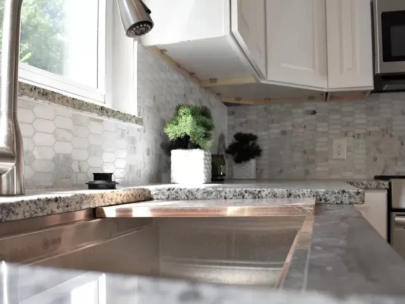 Kitchen countertop with marble backsplash, stainless steel sink, and white cabinets.