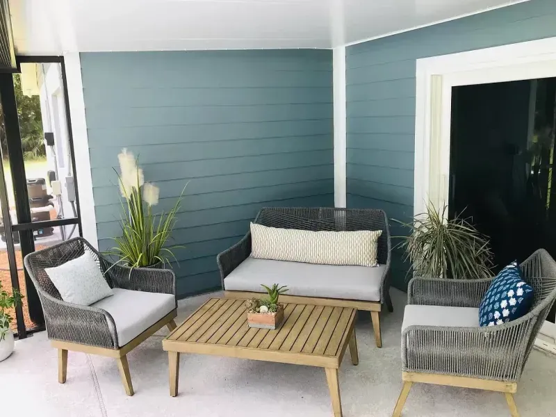 Outdoor seating area with gray rope furniture, wood table, and blue-green wall.