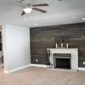 Living room with white walls, wood-plank accent wall, fireplace, and a ceiling fan.