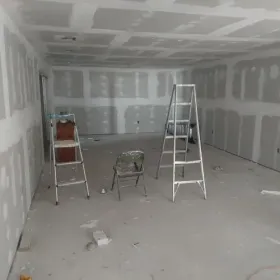 Room under construction with drywall installed on walls and ceiling; ladders and a chair are in the room.