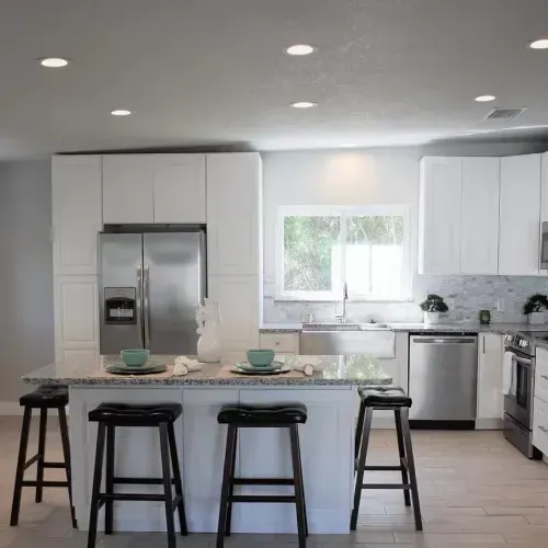 Modern kitchen with white cabinets, stainless steel appliances, and a central island with bar stools.