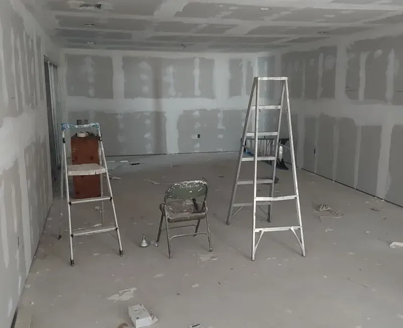 Interior room under construction, with drywall and two ladders. A chair sits in the middle.