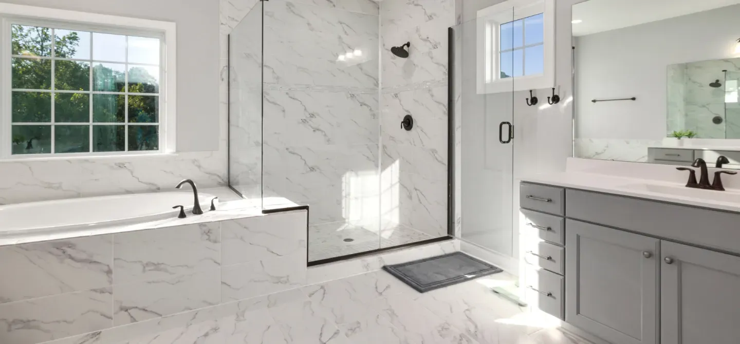 Elegant, modern bathroom with marble tile, a glass shower, soaking tub, and gray vanity.
