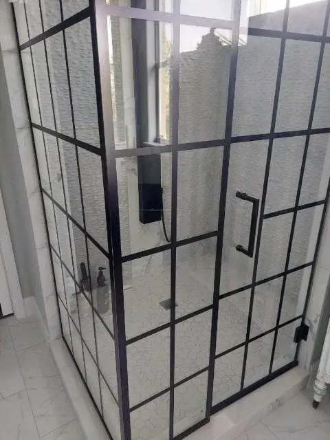 Black-framed shower enclosure with grid design; glass panels and black hardware.