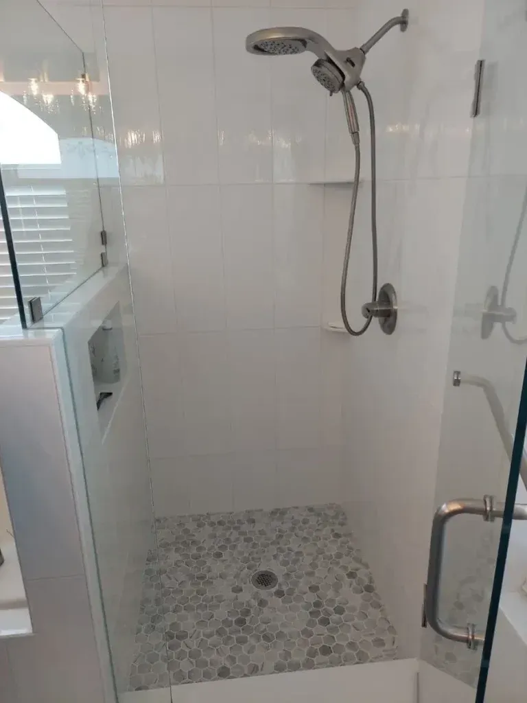 White tiled shower with glass doors and pebble floor. Silver shower head and faucet.